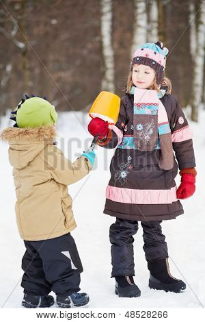 Oudere meisje geeft eskimo gemaakt van sneeuw in plastic emmer en gebroken tak aan jongere kind in de winter 