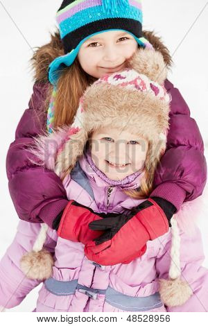 Oudere meisje omarmt haar jongere zus achter staande op sneeuw achtergrond