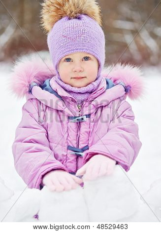 Portret van klein meisje die achter de muur gemaakt van sneeuw blokken in winter park staat
