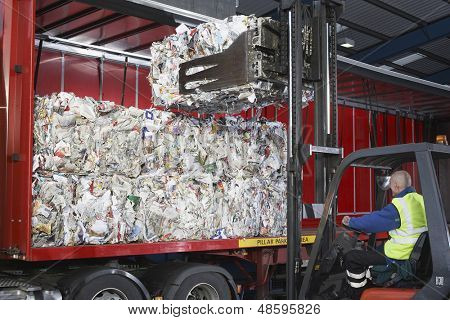 Travailleur au chariot élévateur, chargement des piles de papiers recyclés sur camion