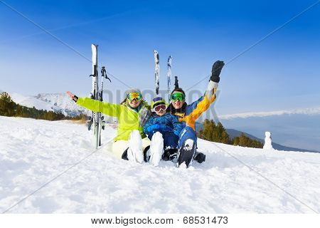 Excited parents and kid in ski masks sit on snow