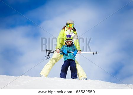 Mother and kid in masks standing with ski polls
