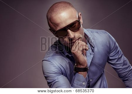 Handsome man in sunglasses sitting thinking with his chin resting on his hand looking down with a pensive expression