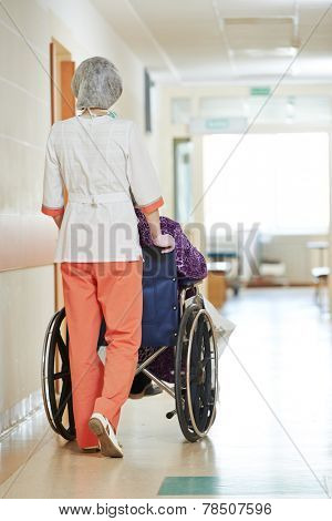 female nurse carer and aged elderly patient woman in wheelchair at clinic hallway