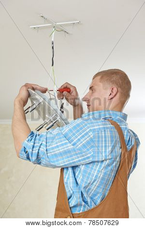 electrician working with cable mounting new wiring and ceiling lamp in home