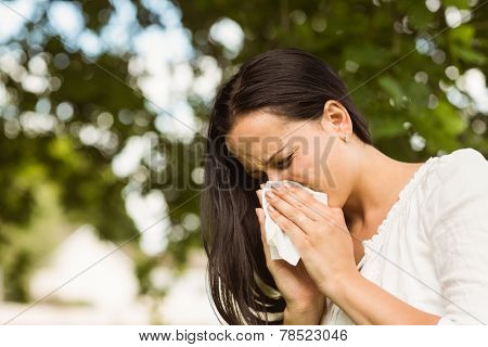Sick brunette blowing her nose in the park