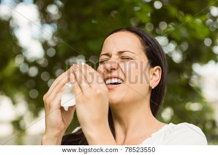 Sick brunette holding tissue sneezing in the park