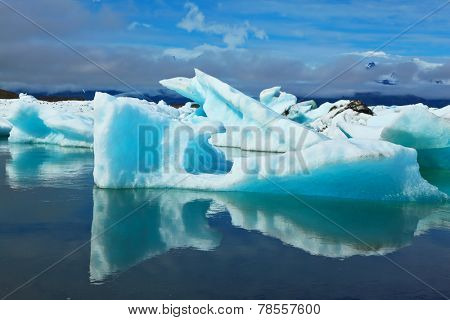 Blue and emerald icebergs and ice floes are reflected in smooth water of the Gulf Yokulsarlon in Iceland. Sunrise.