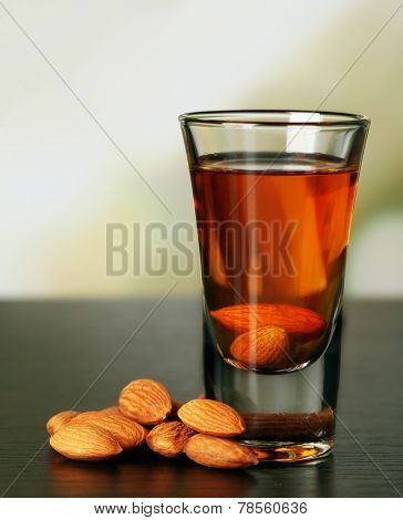Dessert liqueur Amaretto with almond nuts, on wooden table, on light background
