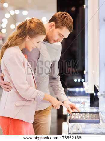 sale, consumerism, shopping and people concept - happy couple choosing engagement ring at jewelry store in mall