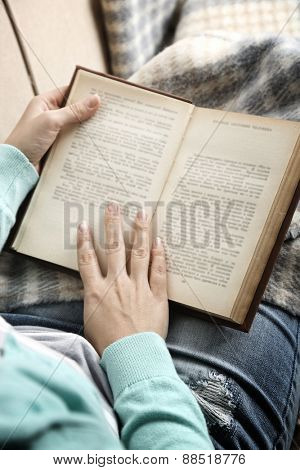 Young woman reading book, close-up, on home interior background