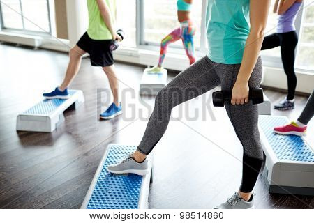 fitness, sport, aerobics and people concept - group of smiling people working out with dumbbells flexing muscles on step platforms in gym