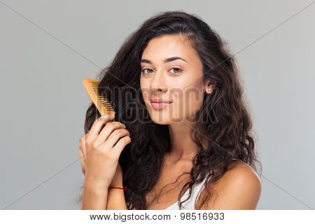Happy cute woman combing her hair over gray background. Looking at camera