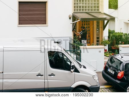 PARIS FRANCE - JUL 12 2017: Young delivery man holding cardboard parcel box ringing at the doorbell and waiting the consignee to open the door and put the signature in clipboard