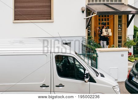 PARIS FRANCE - JUL 12 2017: Young delivery man holding cardboard parcel box knocking ringing at the doorbell and waiting the consignee to open the door and put the signature in clipboard