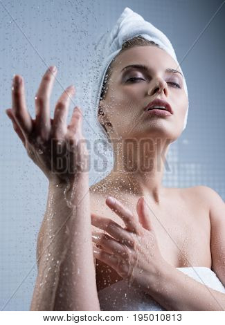 Young pretty girl her head wrapped in towel enjoying water splashes falling on her face