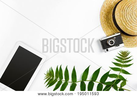 Straw hat with green leaves, tablet and old camera on white background, Summer background. Top view. Copy space. Still life. Flat lay