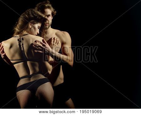 Man and woman in sexy underwear. Couple in love. Macho with muscle biceps triceps hugging sexi girl in fishnet pantyhose on black background. Erotic and desire copy space