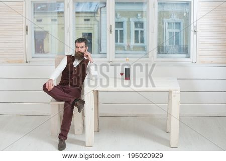 Hipster Sitting On Chair At Table With Bottle And Glass