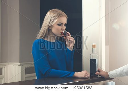 Woman drinking glass of wine at bar. Pretty girl with blond hair fashionable makeup in blue dress with red alcoholic drink. Alcohol appetizer and aperitif. Addictive and convive. Unhealthy lifestyle