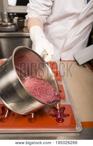 Sweets artisanal production of fruits loly pop at the factory. Close up of the saucepan pan with liquid hot red sugar dispensing to the orange mold. Artisanal production in France