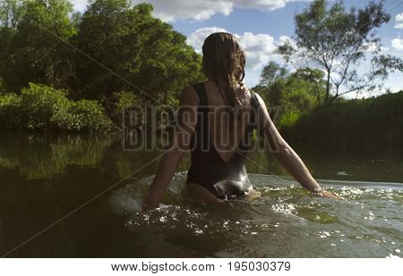 A young woman in a black bathing suit bathing in a forest river