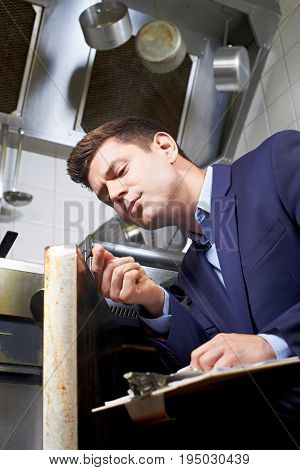 Health Inspector Looking At Oven In Commercial Kitchen
