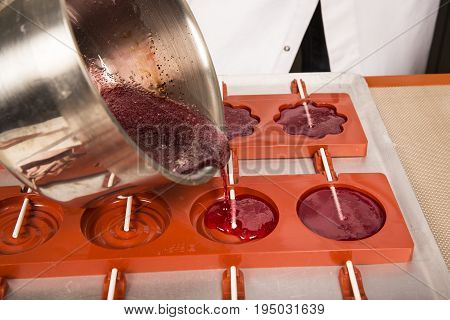 Sweets artisanal production of fruits loly pop at the factory. Close up of the saucepan pan with liquid hot red sugar dispensing to the orange mold. Artisanal production in France