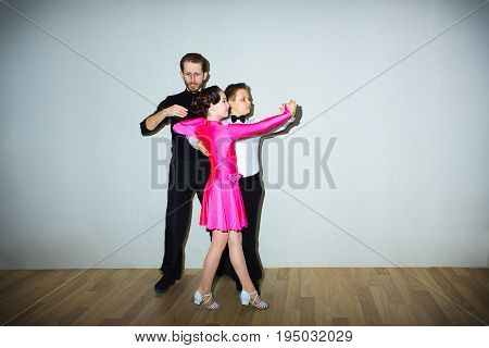 The young boy and girl with male coach or teacher posing at dance studio on gray. The ballroom dancing school and education concept