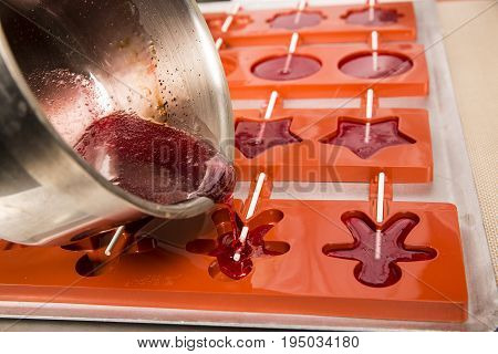 Sweets artisanal production of fruits loly pop at the factory. Close up of the saucepan pan with liquid hot red sugar dispensing to the orange mold. Artisanal production in France