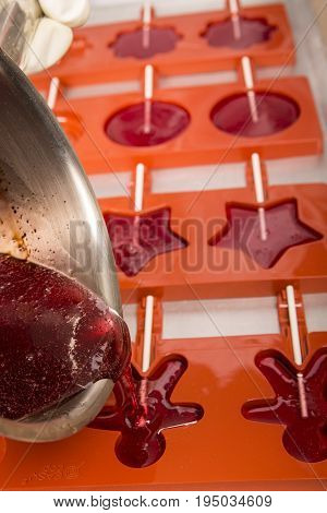 Sweets artisanal production of fruits loly pop at the factory. Close up of the saucepan pan with liquid hot red sugar dispensing to the orange mold. Artisanal production in France