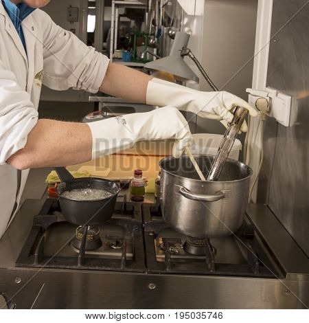 Sweets artisanal production of fruits loly pop at the factory. Close up of the hands of the employee moving the liquid sugar in the pan with spoon and thermometer