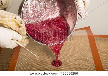 Sweets artisanal production of fruits loly pop at the factory. Close up of the saucepan pan with liquid hot red sugar dispensing to the orange mold. Artisanal production in France