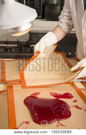 Sweets artisanal production of fruits loly pop at the factory. Close up of the hands of the employee stretching the sugar to make butterscotch fruits candies. Artisanal production in France