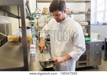 cooking food, baking and people concept - happy male chef cook whipping dough or batter by whisk in bowl at restaurant or bakery kitchen