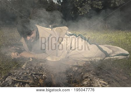 Vagabond young man sleeping in park near illegal fire place