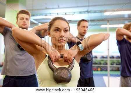 sport, fitness, weightlifting and training concept - group of people with kettlebells and heart-rate trackers exercising in gym