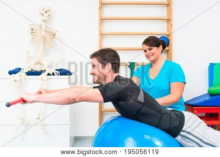 Young man working out in physical therapy on swiss ball with gymnastic stick
