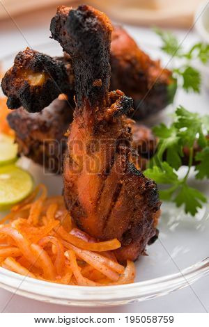 Chicken Tangri kabab or kebab - three Chicken leg pieces marinated with red sauce then grilled and served with salad. It can be served with green chutney
