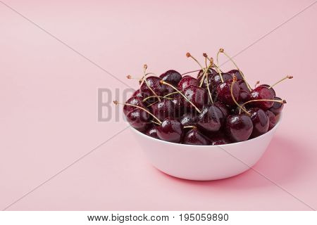White Bowl Of Fresh Red Cherries On A Pink Background. Copy Space. Close-up