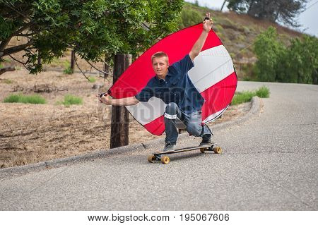 Daredevil skateboarder man holding parachute to control speed as he moves downhill.