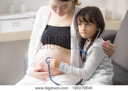 Little cute girl using stethoscope check stomach to her mother.
