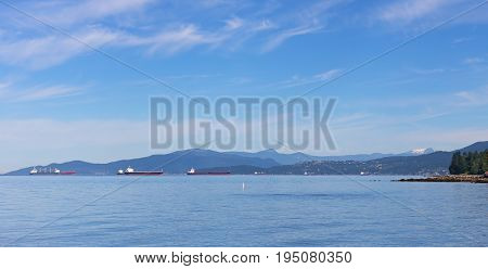 Sea landscape in summer with ships and mountains on horizon in Vancouver Canada. Ships in the roadstead along sea coast.