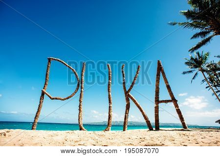 Puka Beach Boracay Philippines. Big wooden sign on the beach sand. Blue sky and ocean on the background.