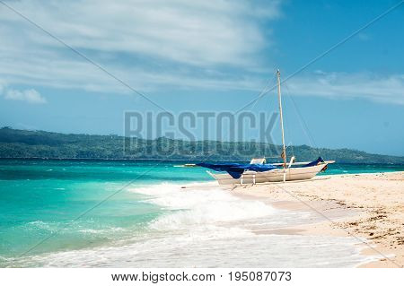 Philippine traditional boat with blue sail on the tropical beach. Boracay. Blue bright sky with clouds ocean with waves white sand.