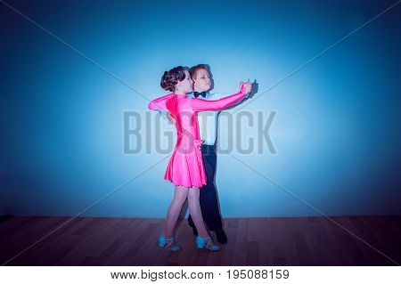 The young boy and girl posing at dance studio on blue in tango posture. The ballroom dancing concept