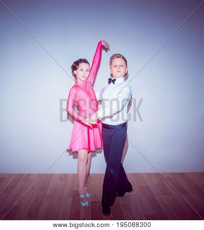 The young boy and girl posing at dance studio on blue in tango posture. The ballroom dancing concept