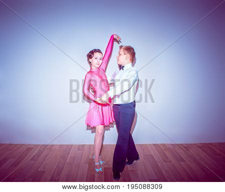 The young boy and girl posing at dance studio on blue in tango posture. The ballroom dancing concept