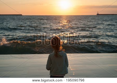 dreaming little girl with hair lit by warm sunlight looking at the sea sunset in autumn