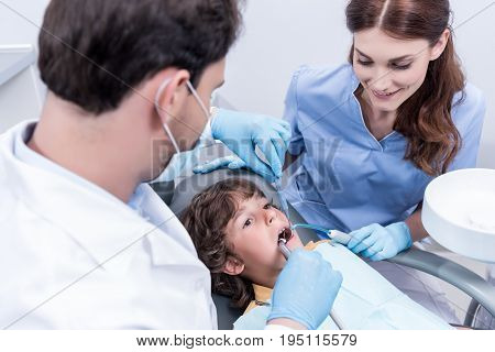 Dentists Treating Teeth Of Little Patient In Dentist Chair In Hospital